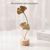 A golden ginkgo leaf metal decorative sculpture with a slender stem standing on a round wooden base.
