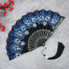 A dark blue and white floral patterned antique folding fan displayed on a gray surface.