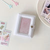 A white compact star-shaped photo card holder album with a pink cover and a clear window is displayed on a light surface.