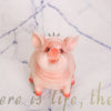 A cute pink resin piggy bank with large ears sitting on a white surface.