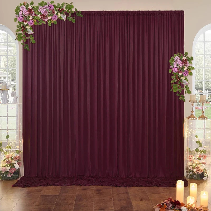 A deep burgundy fabric backdrop curtain with floral greenery accents, set in a room with arched windows.