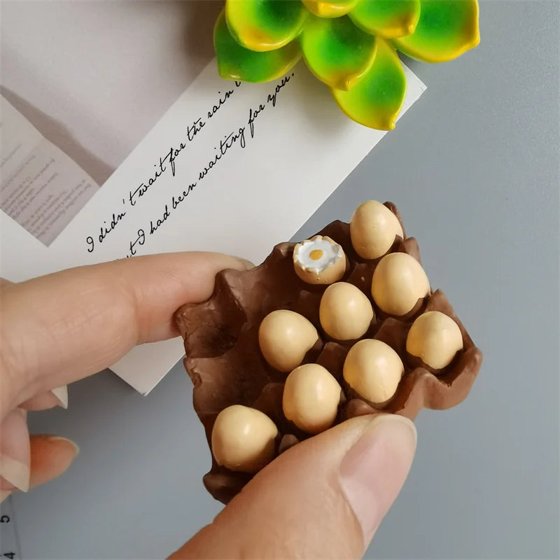 A hand holds a brown food-shaped magnet with small, round, light-colored edible decorations against a white background.