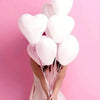 A person holds a bouquet of white heart-shaped latex balloons against a pink background.