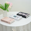 A stack of white and faded books next to a vase of pink and white flowers on a white table.