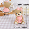 A light brown baby bear cake topper with a pink bow and dress, shown from the back.