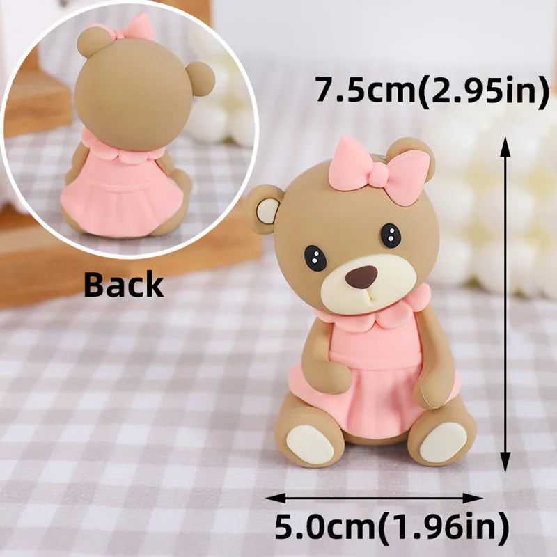 A light brown baby bear cake topper with a pink bow and dress, shown from the back.
