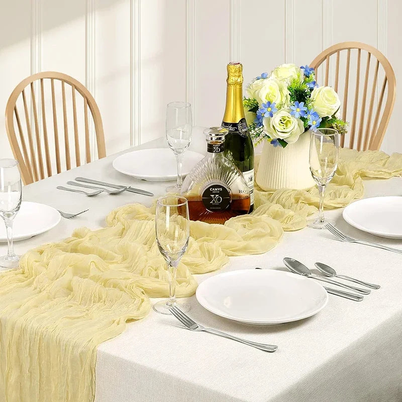 A white table set featuring a sage green gauze table runner, white plates, silverware, and a glass of sparkling wine with a f