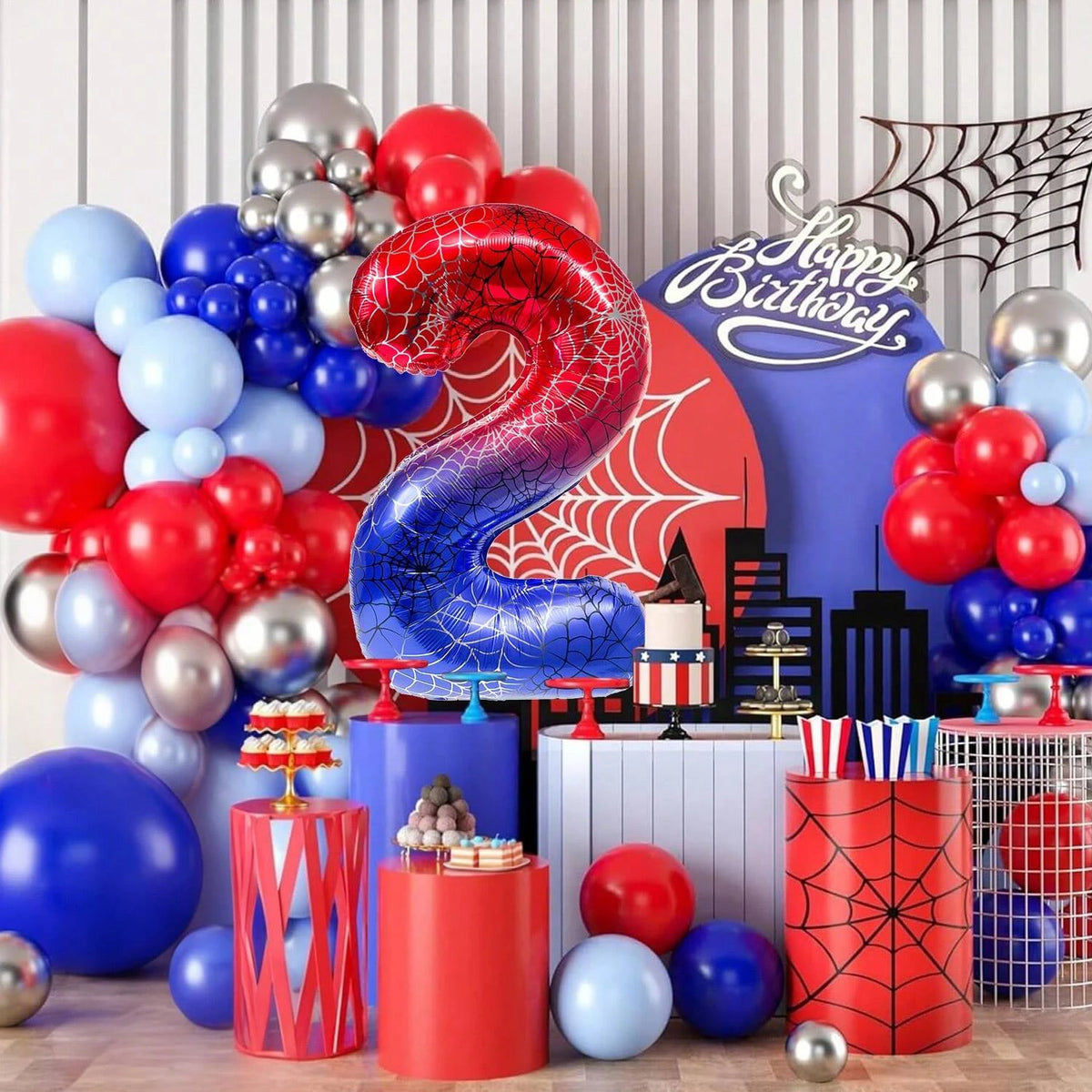 A vibrant birthday party decoration featuring a large red and blue spiderweb foil balloon surrounded by various colored ballo