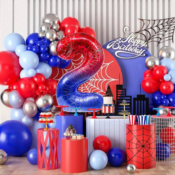 A vibrant birthday party decoration featuring a large red and blue spiderweb foil balloon surrounded by various colored ballo