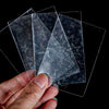 A hand holds several holographic card sleeves, clear plastic protectors with star patterns, against a black background.