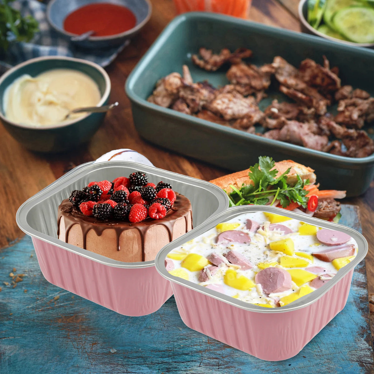 Pink reusable aluminum foil baking cups with lids and spoons filled with fruit and meat