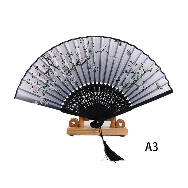 Elegant black lace folding hand fan with silver floral embroidery displayed on a wooden stand.