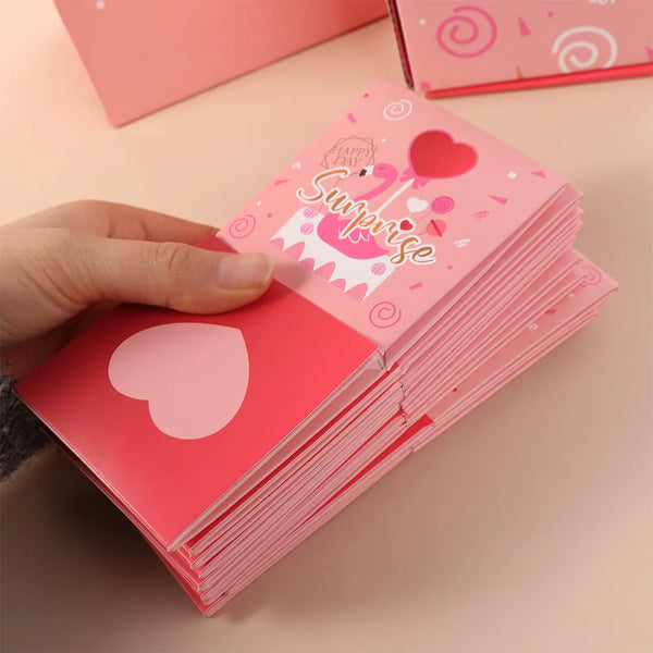 A hand holds a stack of pink pop-up surprise gift boxes with heart designs on a light background.