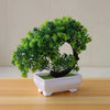 A vibrant green artificial bonsai tree decoration planted in a white rectangular pot on a wooden surface.
