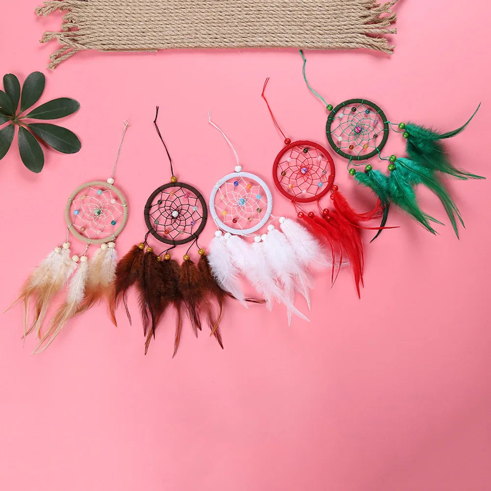 A collection of handmade feather dreamcatchers in various colors including pink, red, and green, displayed on a pink backgrou
