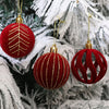 A close-up of velvet red Christmas tree ornaments with gold accents hanging on a white frosted pine branch.