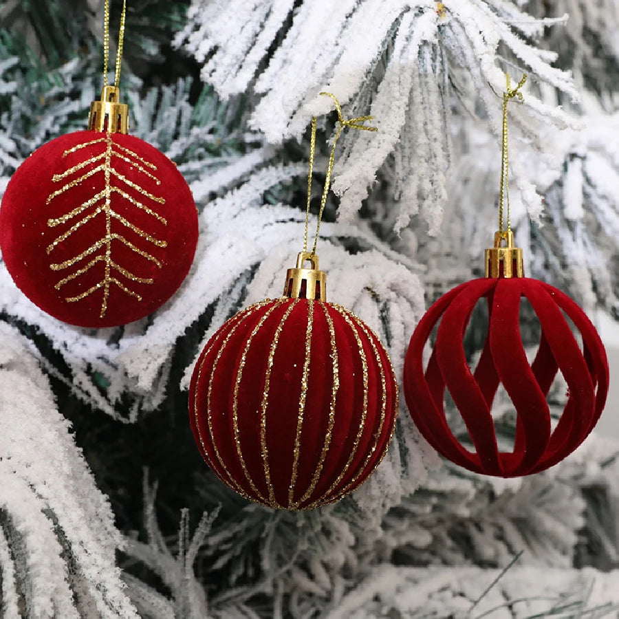 A close-up of velvet red Christmas tree ornaments with gold accents hanging on a white frosted pine branch.