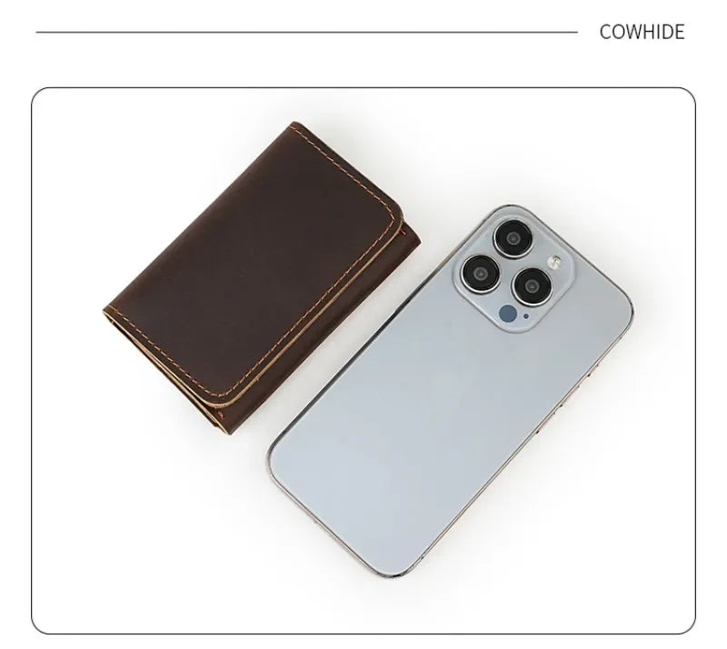 A dark brown vintage leather card holder and cable organizer next to a silver smartphone.