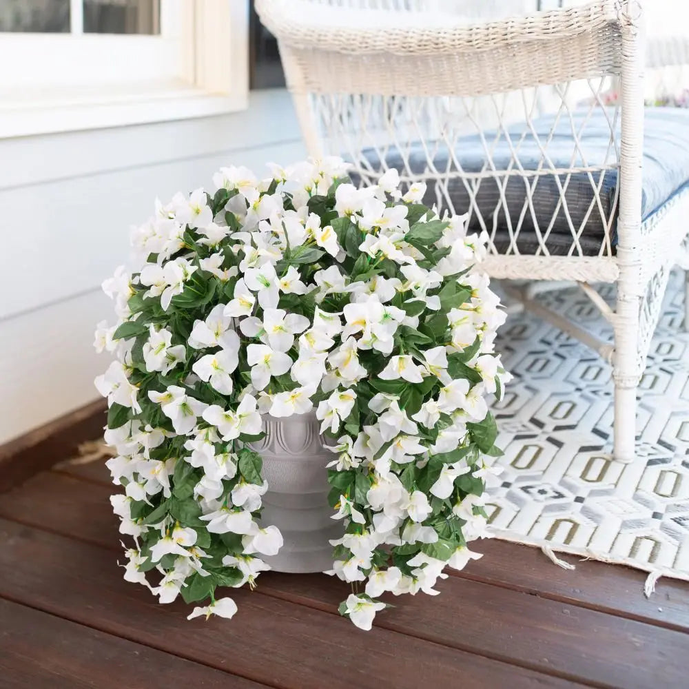 A lush arrangement of white faux bougainvillea vine flowers in a gray vase on a wooden deck.