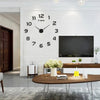 A giant black acrylic wall clock with Roman numerals and hands is mounted on a white brick wall above a wooden console table.