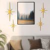 A set of four gold metal star wall art pieces displayed on a light gray wall above a sofa.