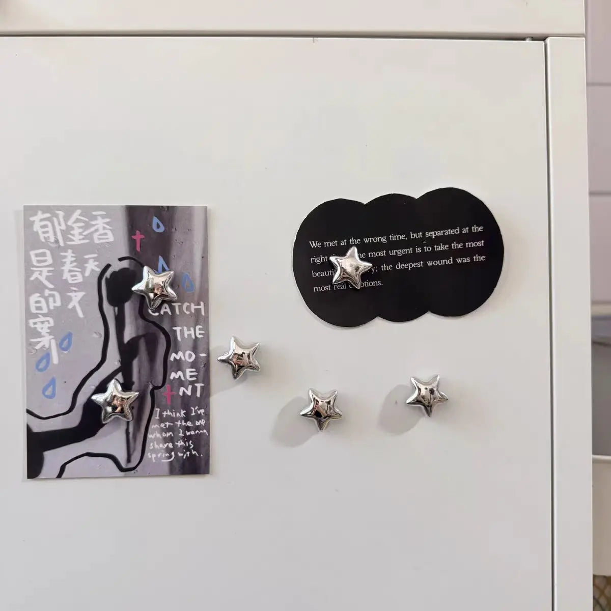 A display of decorative fridge magnets featuring silver star designs and a black circular text magnet.
