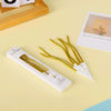 A set of six metallic twisted coil birthday candles in gold and white are displayed on a light yellow surface.