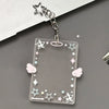 A clear acrylic photocard holder with stars, lines, and wings is attached to a silver keychain.