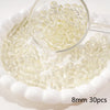 A clear glass measuring spoon holds small round beads scattered on a white dish.