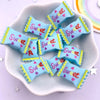A white dish holds several pastel blue and pink heart-shaped candy resin cabochons with yellow edges.