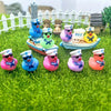 A collection of mini resin cruise ducks with sunglasses in various colors resting on green grass.