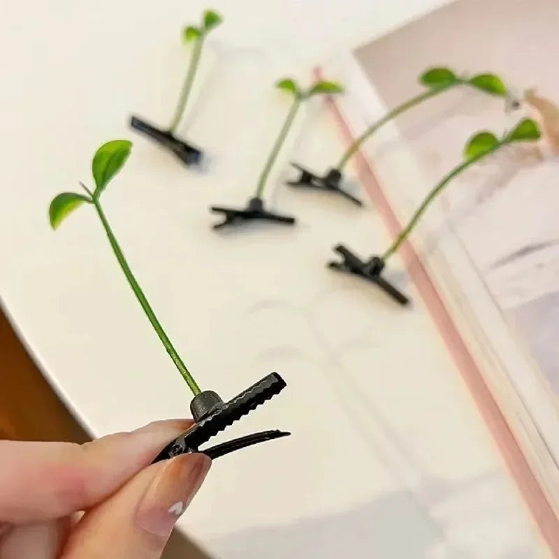 A hand holds a black bean sprout hair clip with a grass top, showing several similar clips on a white surface.
