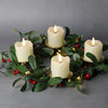 A wreath of green leaves and red berries decorated with white pillar candles lit by warm LED lights.