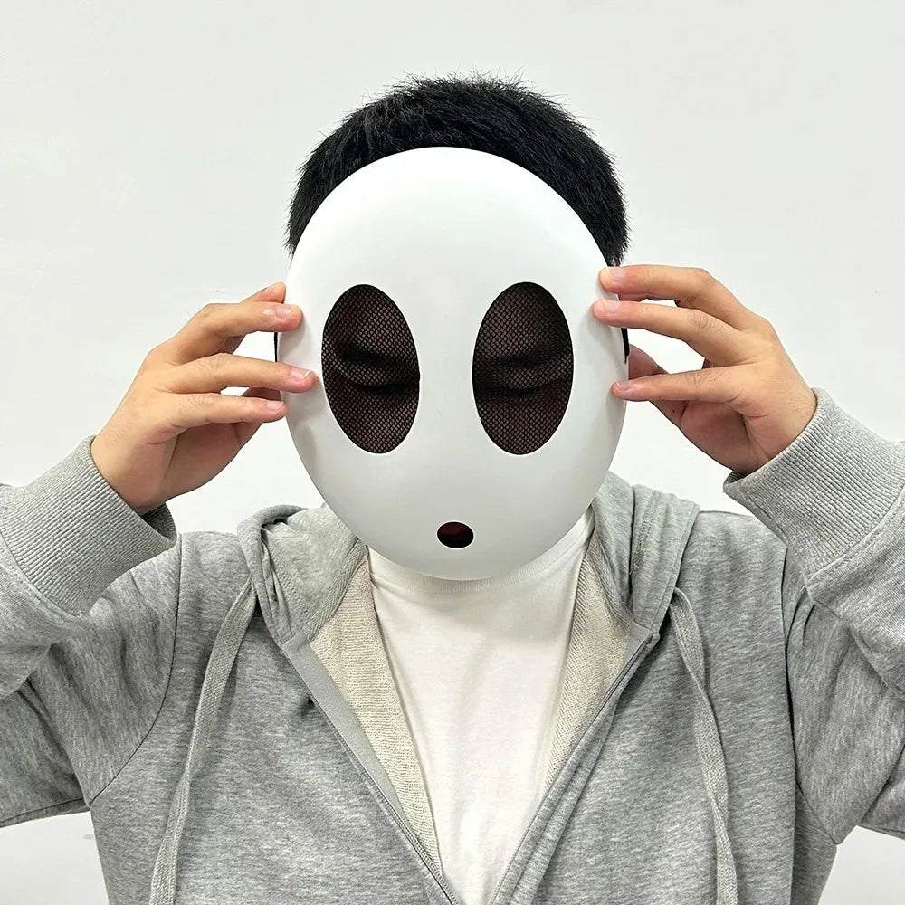 A person is holding a white, smooth mask resembling a face with large black eye holes.