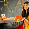 A smiling woman holds a bouquet of orange and yellow marigold flowers against a dark gray background.