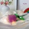 A translucent pink rose flower building block in a green stem is displayed on white fabric.