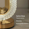 A close-up view of an oval crystal LED table lamp with a gold finish and diamond-cut glass shade.