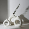 Three white ceramic circular vases with a delicate green branch arrangement on a light surface.