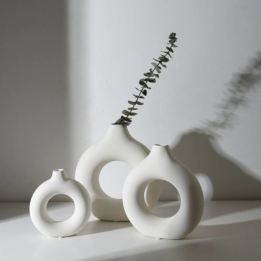 Three white ceramic circular vases with a delicate green branch arrangement on a light surface.