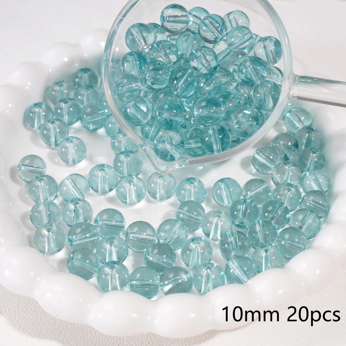 A clear glass dropper holds small blue beads, with many more scattered on a white dish.