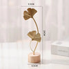 A golden ginkgo leaf metal decorative sculpture standing on a round wooden base.