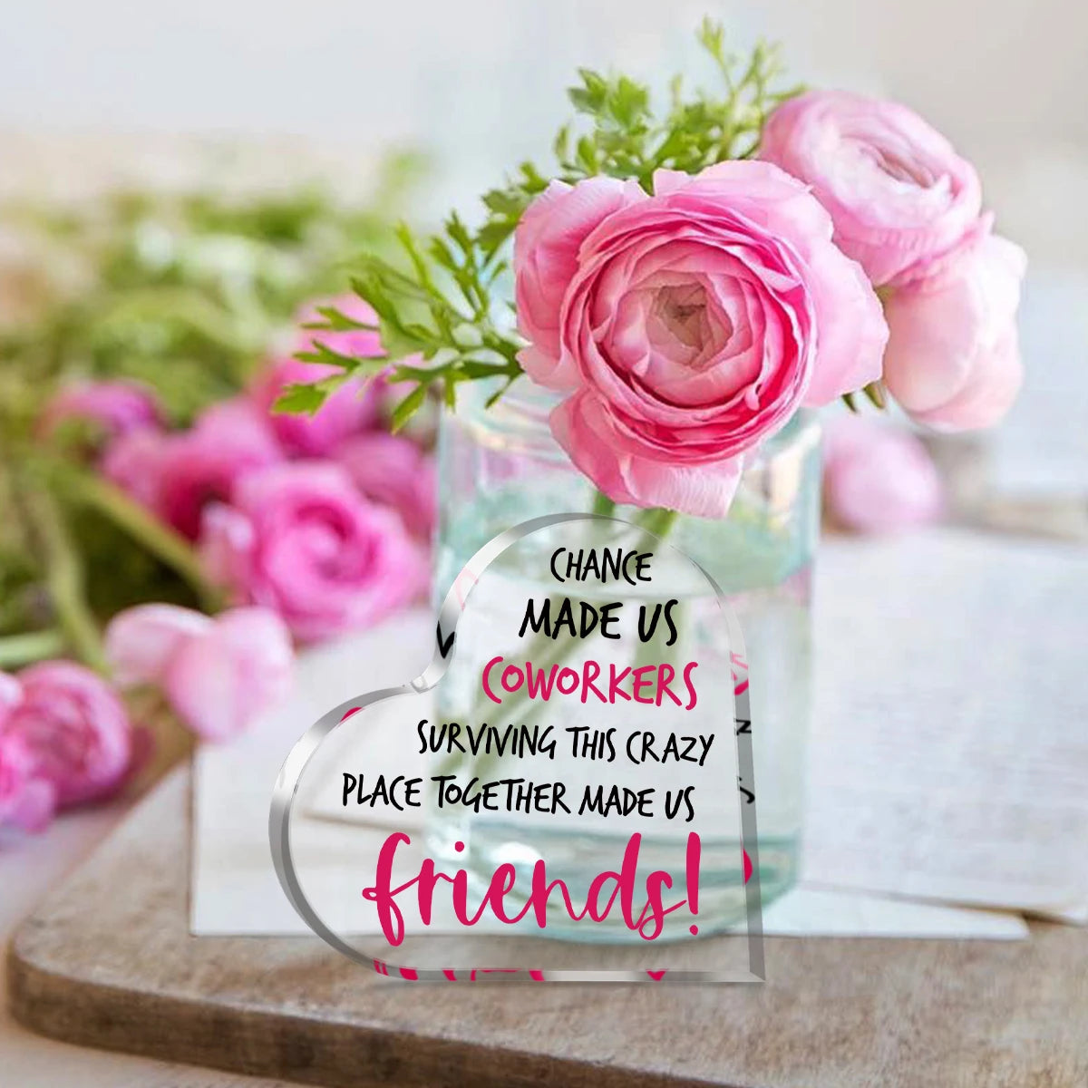 A heart-shaped glass vase filled with pink roses and a message that says Chance made us coworkers surviving this crazy place 