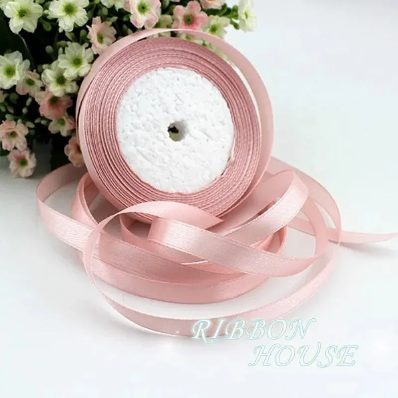 Pink silk satin ribbon roll with white filling and loose ribbons on a white background