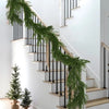 A realistic green Norfolk pine garland draped along a modern white staircase with black railings.