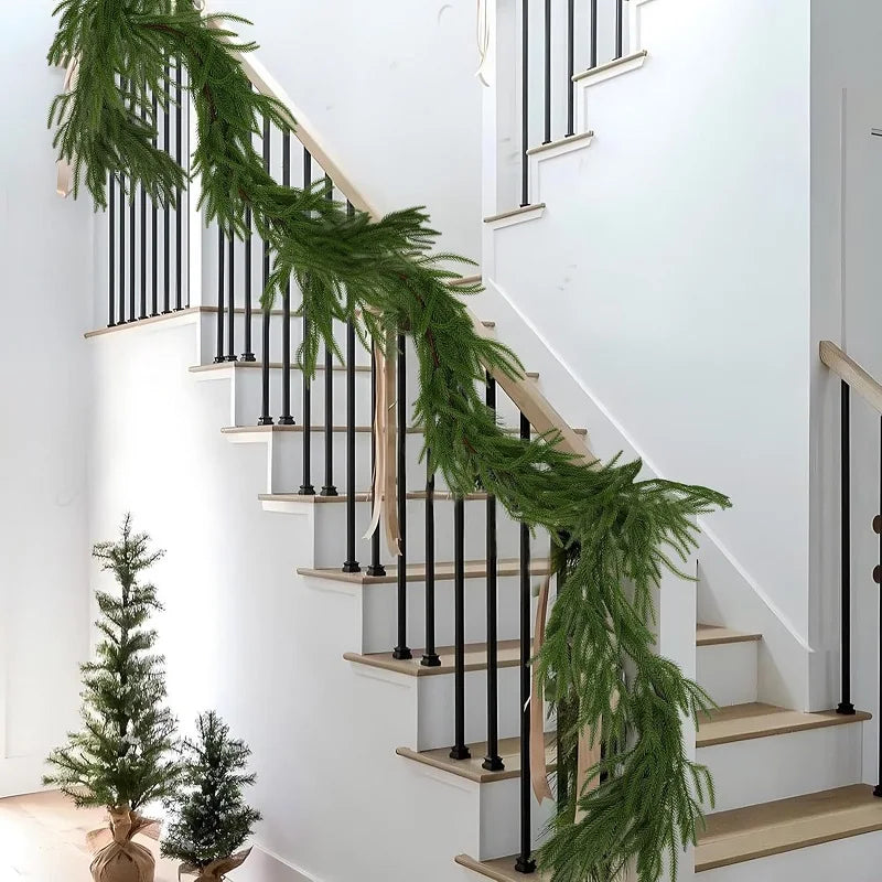 A realistic green Norfolk pine garland draped along a modern white staircase with black railings.