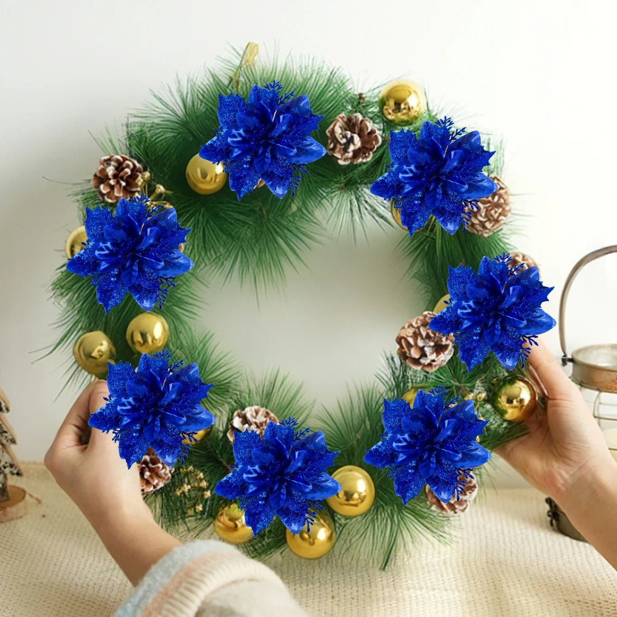 A wreath of blue glitter artificial poinsettia flowers and pinecones decorated with gold ornaments.