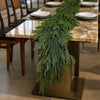 An artificial Norfolk pine garland with warm white lights displayed on a wooden table.