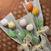 A bouquet of handmade crochet tulips in orange and yellow colors arranged on green stems and presented in clear packaging.