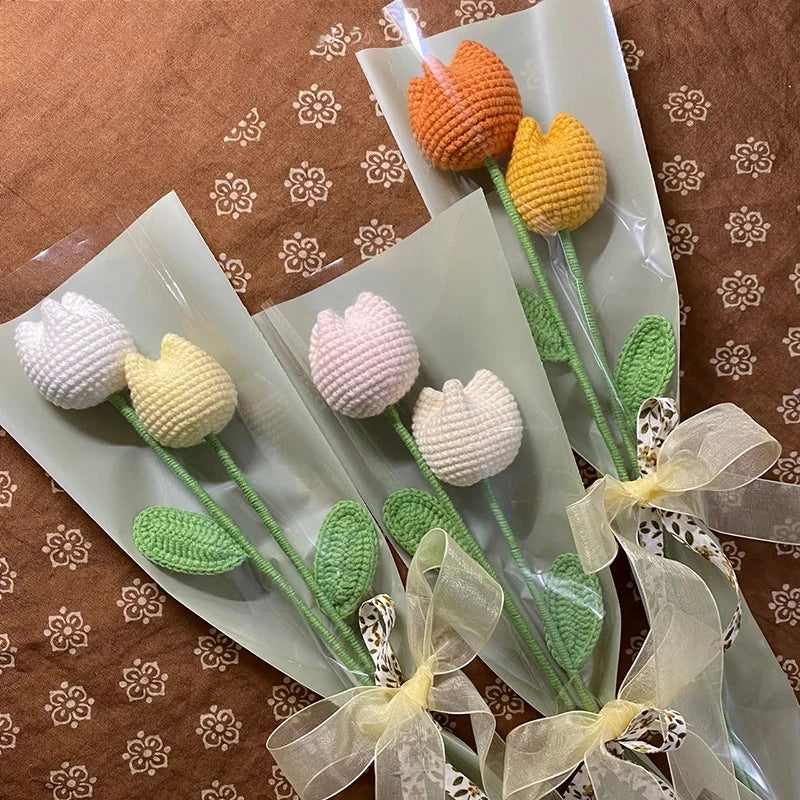 A bouquet of handmade crochet tulips in orange and yellow colors arranged on green stems and presented in clear packaging.
