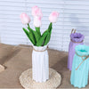 Modern white plastic vase with a basket design holding pink tulips on a woven mat.
